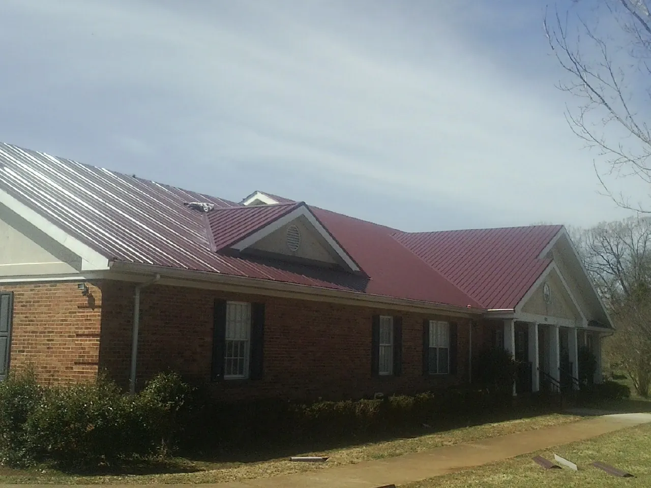 Red metal roof with gabled entries on a long brick building, from a Hail Damage Roof Repair job in Cedar Hill